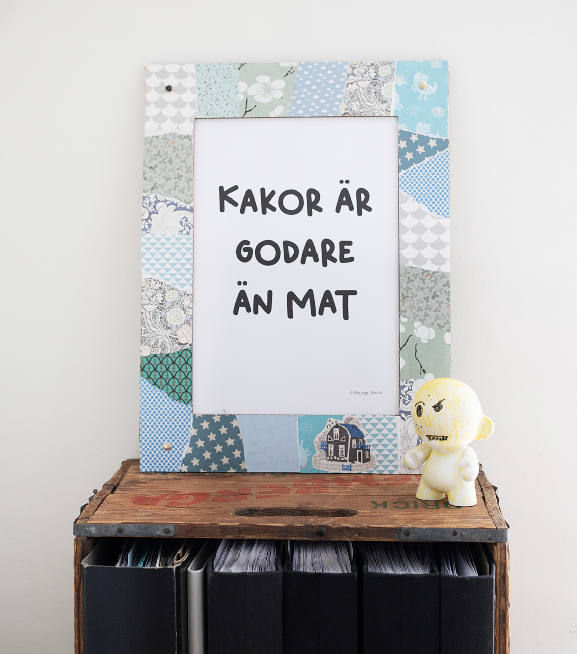 En dekorerad kartongram på en hylla med en poster med texten Kakor är godare än mat.
